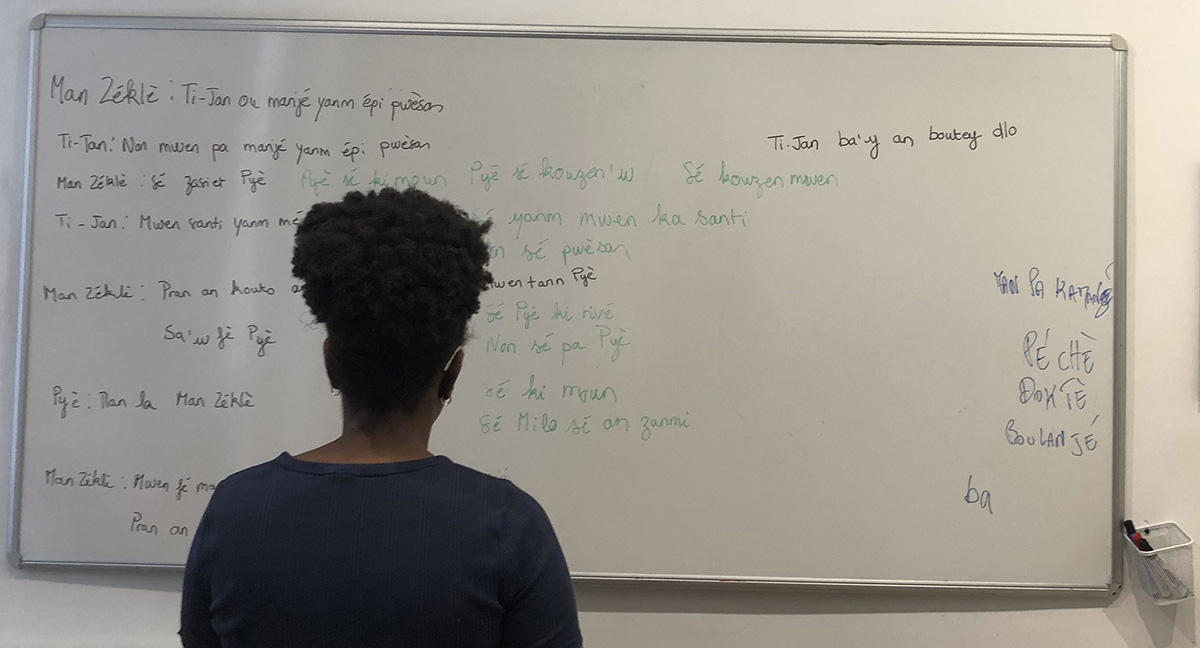Participant d'un cours de créole au Kréyol Akademi écrivant des phrases en langue créole devant un tableau blanc